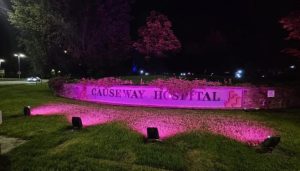 An outdoor entrance sign at Causeway Hospital illuminated in pink light.