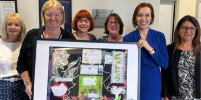 A group of women, including Trust Board Chair Anne O'Reilly and Chief Executive Jennifer Welsh, standing together holding a framed piece of art.