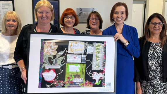 A group of women, including Trust Board Chair Anne O'Reilly and Chief Executive Jennifer Welsh, standing together holding a framed piece of art.