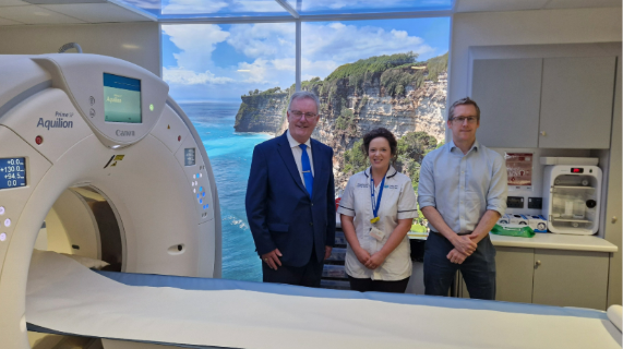 Three people standing beside a scanning machine.