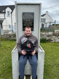 A service user from Mountfern sits on a stone chair on Rathlin Island.