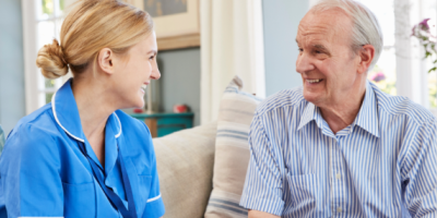 A nurse wearing a blue tunic talks to an older man.