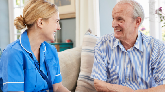 A nurse wearing a blue tunic talks to an older man.