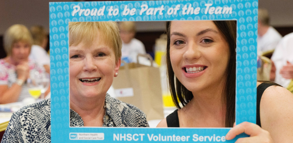 Two women smiling through a selfie frame with text on it which reads 'proud to be part of the tean, NHSCT volunteer service'.