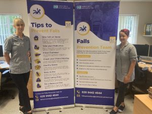 Two staff members standing beside pop-up stands which feature falls prevention information.