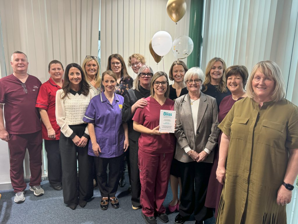 A large group of people standing together. Some are wearing healthcare uniforms. One is holding a small plaque.