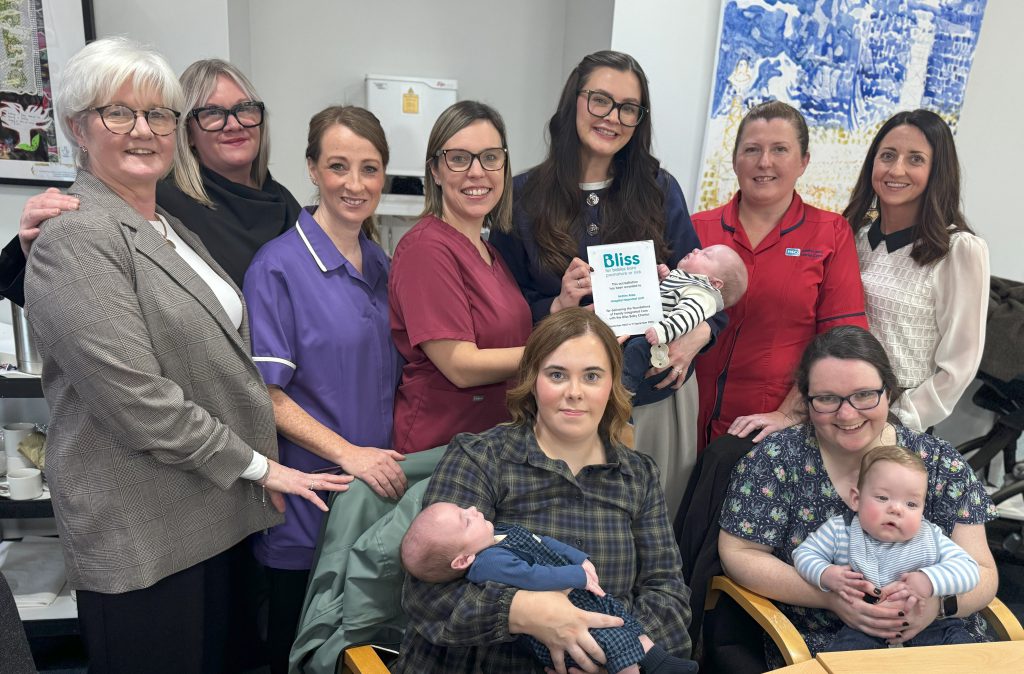 A group of people, including three babies. Some are sitting, some are standing. One person is holding a small plaque.