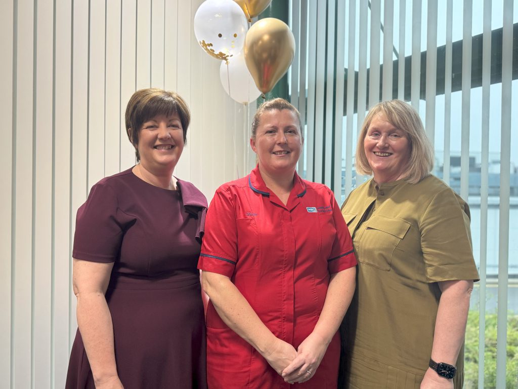 Three people standing together. One is wearing a red nursing tunic.