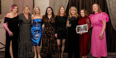 Eight women standing together. One is holding a glass trophy while another is holding a framed certificate.