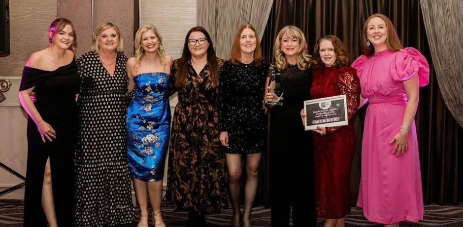 Eight women standing together. One is holding a glass trophy while another is holding a framed certificate.