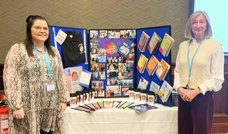 Two women standing beside a display board and a table with information resources.