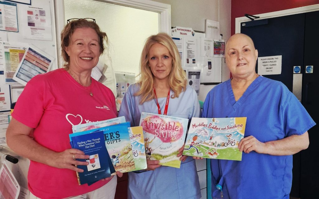 Three healthcare workers standing together in a hospital setting, holding books.