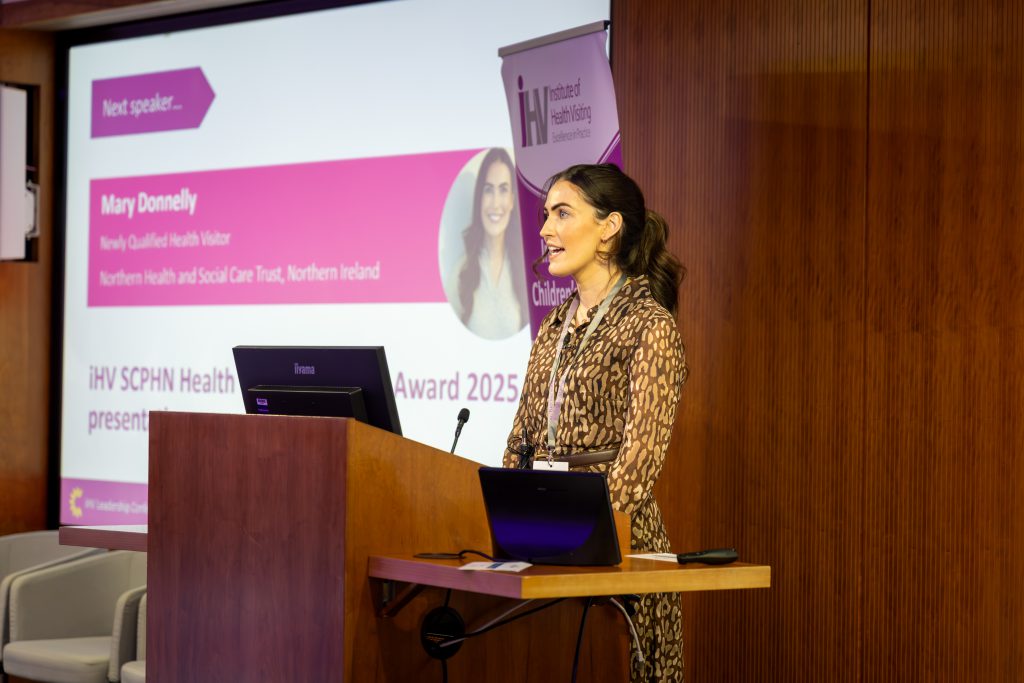 A woman stands at a podium with a projector screen behind her.