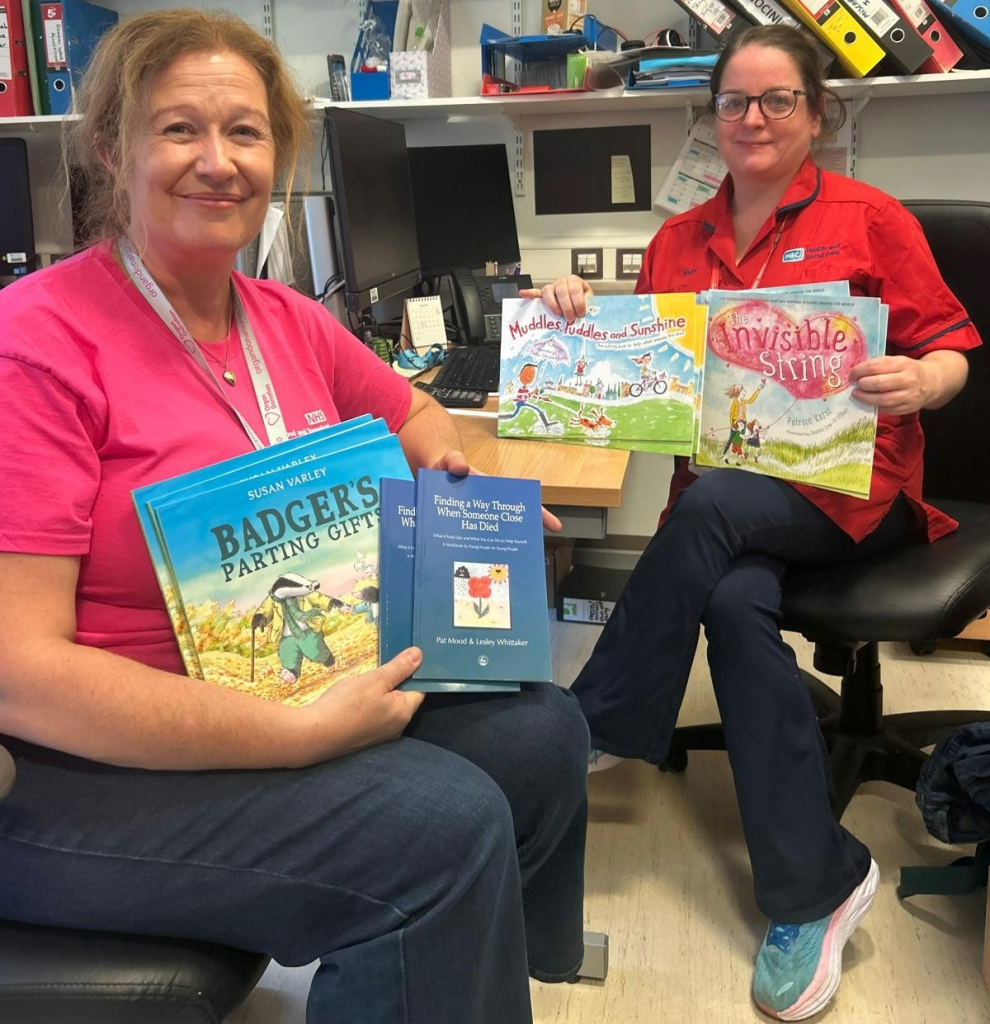 Two healthcare workers sitting together in an office setting, holding books.
