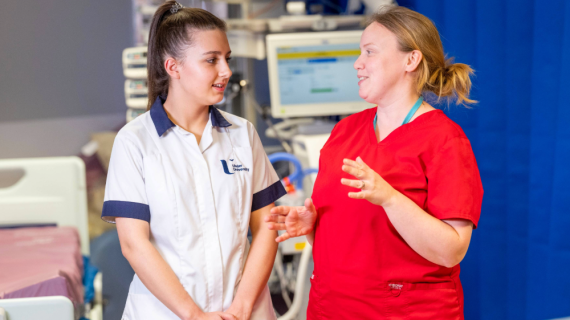Two HSC workers chatting to each other in award. One is wearing a white student's tunic and the other is wearing a red tunic
