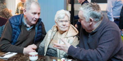 Three older people talking to each other while sitting at a table.