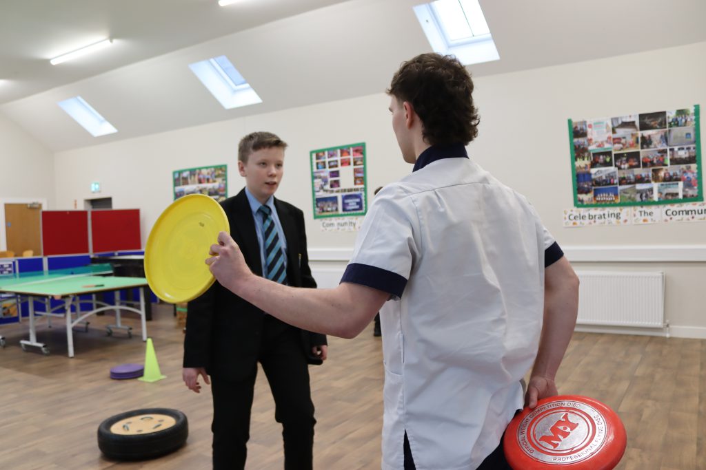 A school pupil playing a game with an OT student. The student is holding colourful circular discs.