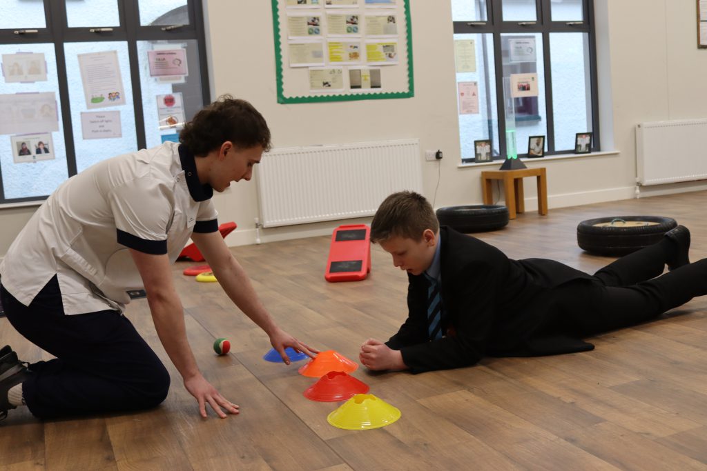 A school pupil playing a game with an OT student. The school pupils is lying on the floor on his front.