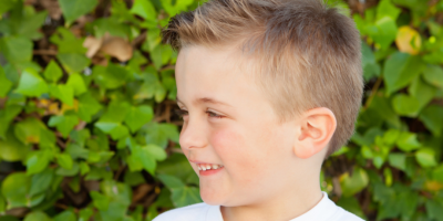 Profile view of a young boy, with a green hedge behind him.