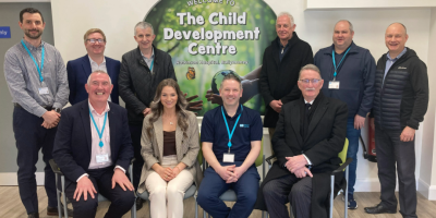 A group of people, some standing, some seating, with a sign on the wall behind them for the Child Development Centre.
