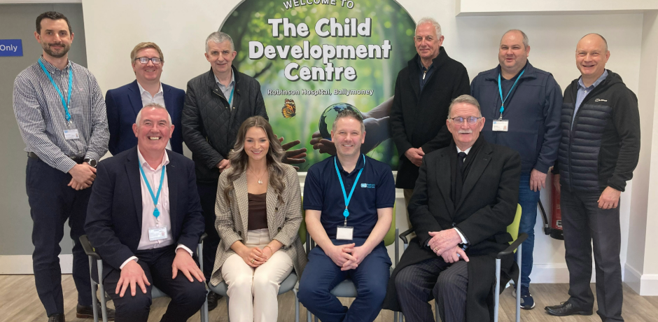 A group of people, some standing, some seating, with a sign on the wall behind them for the Child Development Centre.