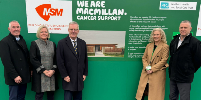 Five people standing in front of green hoarding, featuring logos for Macmillan, MSM, and the Northern Trust along with an artist's impression of the new Macmillam centre.