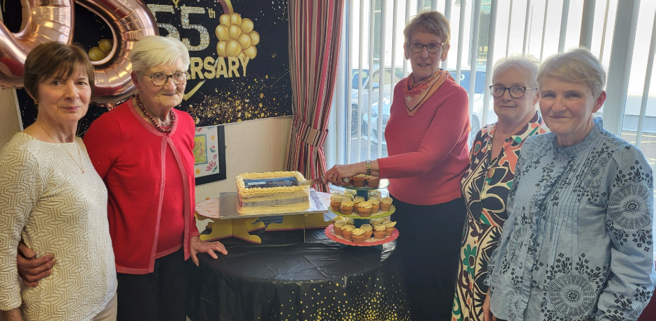 Five people stand around a table with a celebration cake.