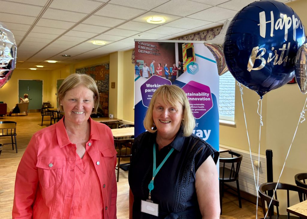 Trust Chair Anne O'Reilly and Chief Executive Suzanne Pullins, with a 'Happy Birthday' balloon and a Causeway Hospital pop-up banner in the background.