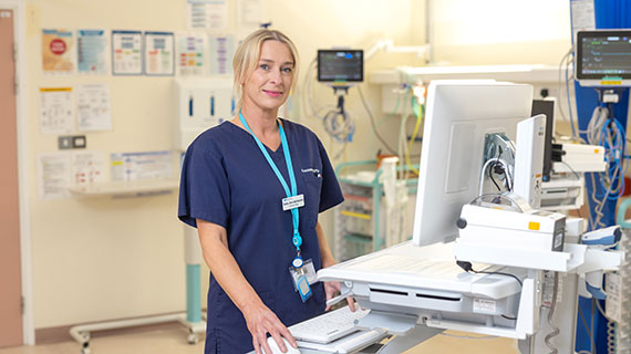A Health And Social Care Staff Member In Dark Navy Uniform Beside A Computer