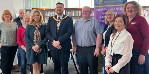 A group of people, including a Council representative wearing a chain, standing in a library with pop-up banners behind them.