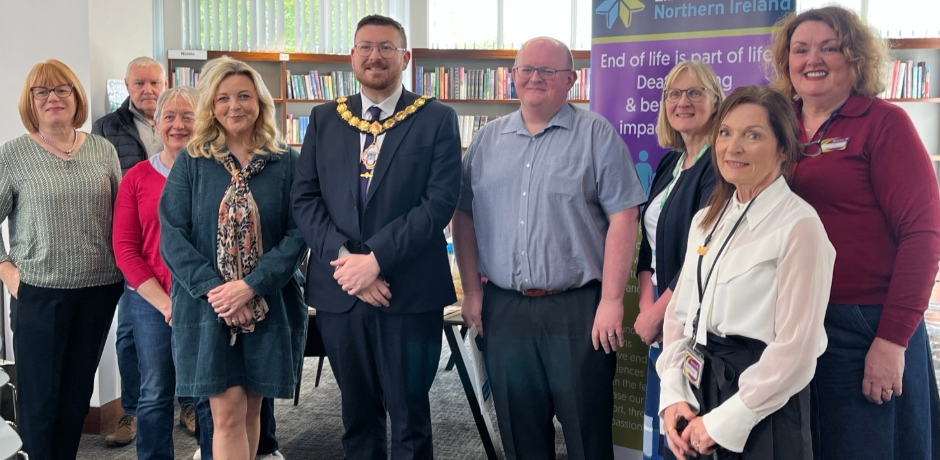 A group of people, including a Council representative wearing a chain, standing in a library with pop-up banners behind them.