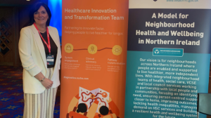 A woman stands beside two pop up banners about neighbourhood health and wellbeing and healthcare innovation.