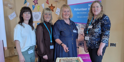Four women stand in front of a table, preparing to cut a large cake.
