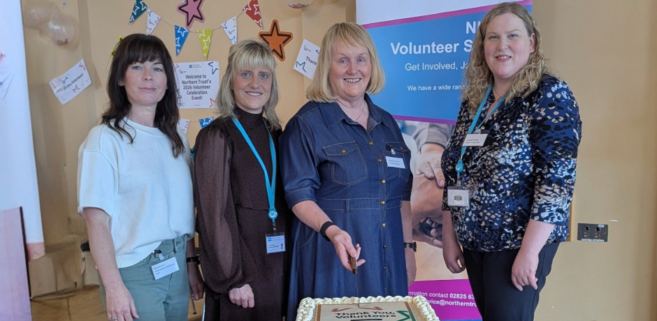 Four women stand in front of a table, preparing to cut a large cake.