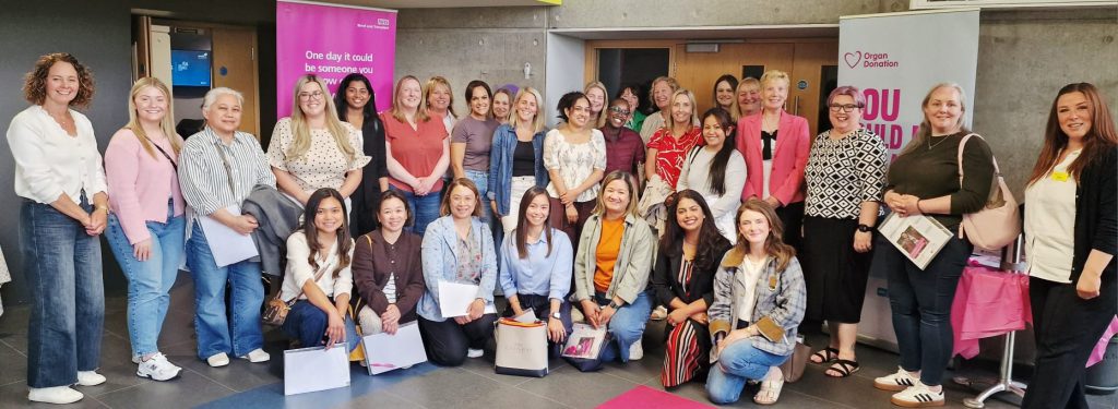 A large group of women, some kneeling, some standing, with a pop-up banner about organ donation behind them.