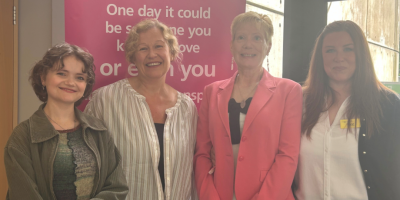 Four women standing together, with an organ donation pop-up banner behind them.