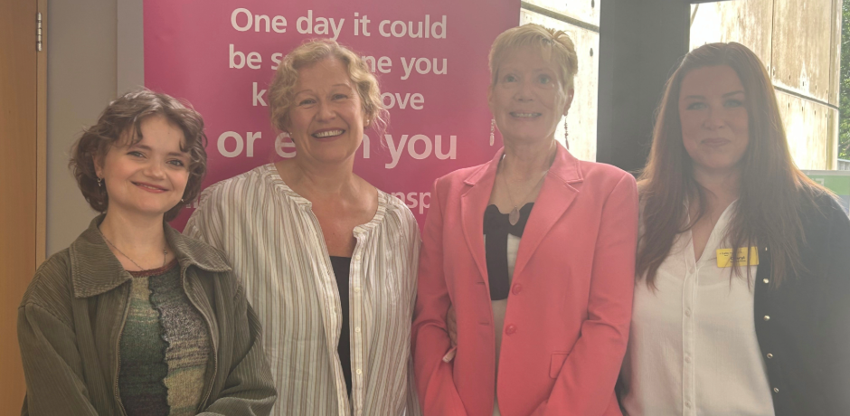 Four women standing together, with an organ donation pop-up banner behind them.
