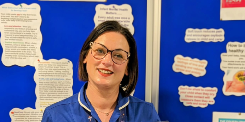 Neonatal Clinical Sister Leanne Richmond stands in front of an information board.