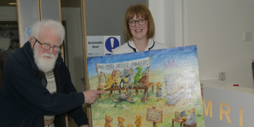 Artist Brian Willis stands beside radiographer Lesley Thompson, who is holding the MRI Noisemakers painting.