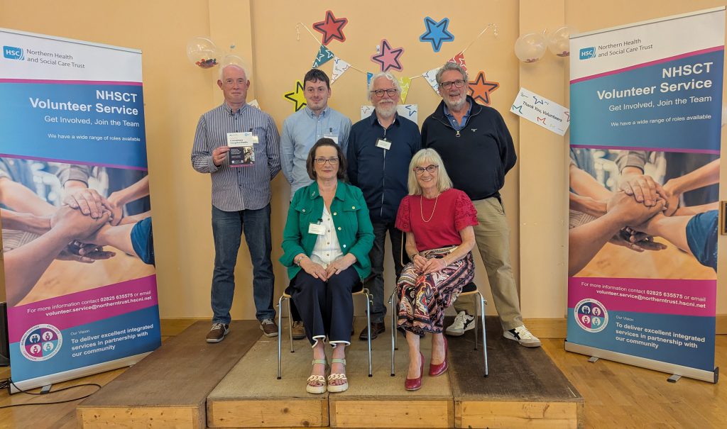 A group of volunteers, some sitting, some standing, with pop-up banners about volunteering either side.
