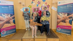A group of volunteers, some sitting, some standing, with pop-up banners about volunteering either side.