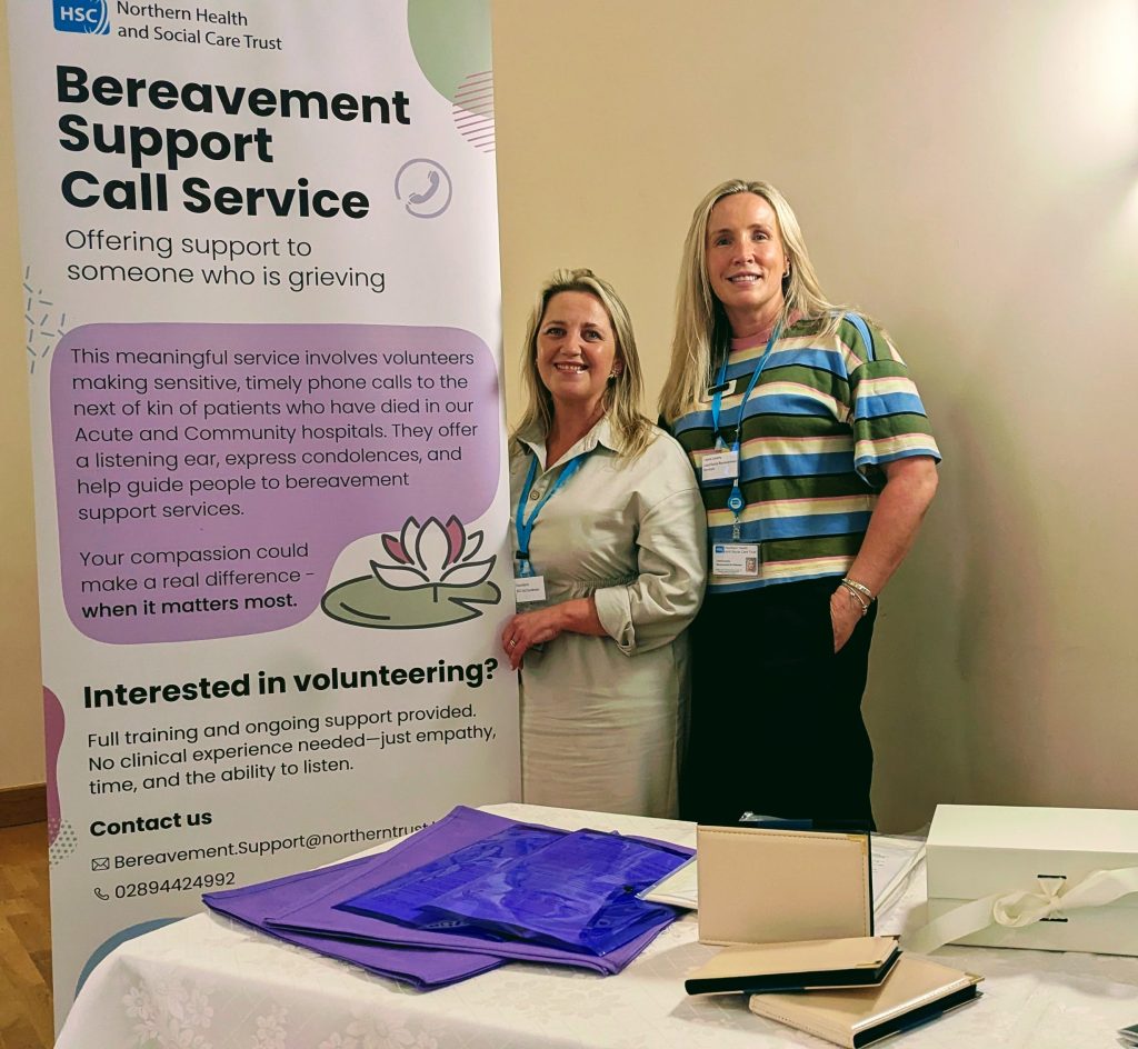 Two women stand beside a pop-up about bereavement support call service.