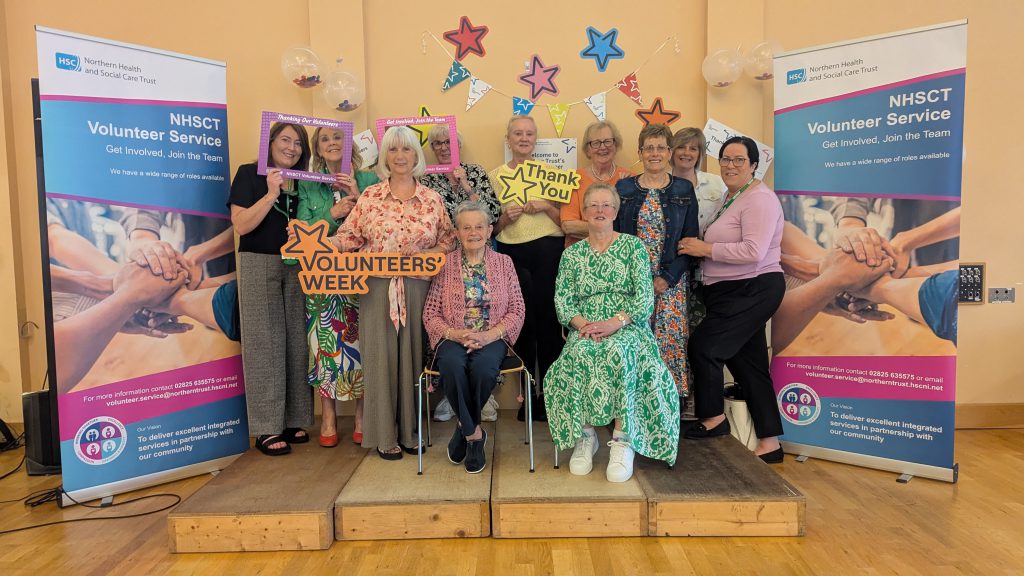 A group of volunteers, some sitting, some standing, with pop-up banners about volunteering either side.