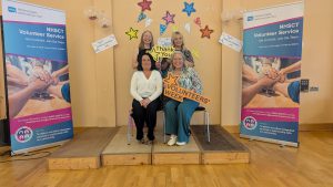 A group of volunteers, some sitting, some standing, with pop-up banners about volunteering either side.