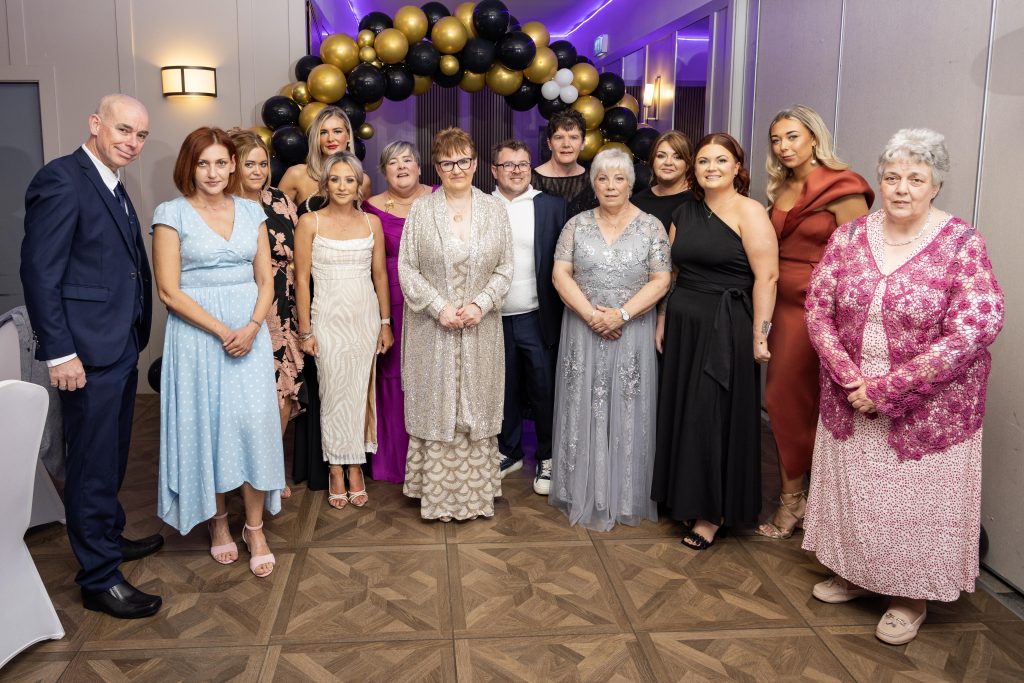 A group of people stand in front of a balloon arch, dressed for a formal occasion. 