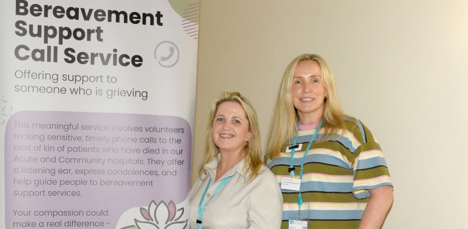 Two women standing in front of a Bereavement Support Call Service promotional banner at a table with purple folders.