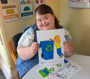 A service user holds up a colouring page showing a recycling bin.