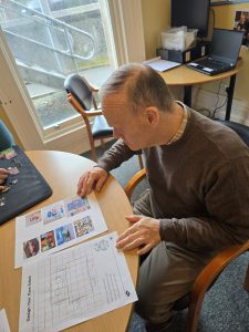 A service user sits at a table, looking at pages about designing a robot.