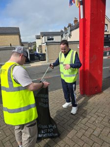 Two men wearing high viz vests, litter picking.