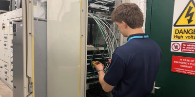 A man stand working at an electrical cabinet.
